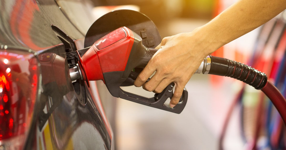 A close-up of a person holding a gas station pump nozzle and pumping fuel into the tank of their vehicle.