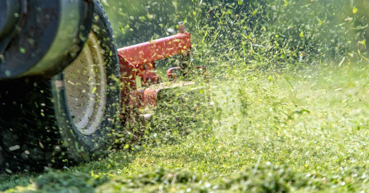 The base of a riding lawnmower maneuvering through a field, cutting grass and sending it flying through the air.