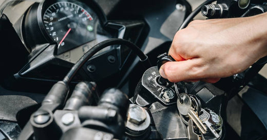 A motorcyclist inserts the key into the bike’s ignition, preparing to start the engine. The vehicle is black.