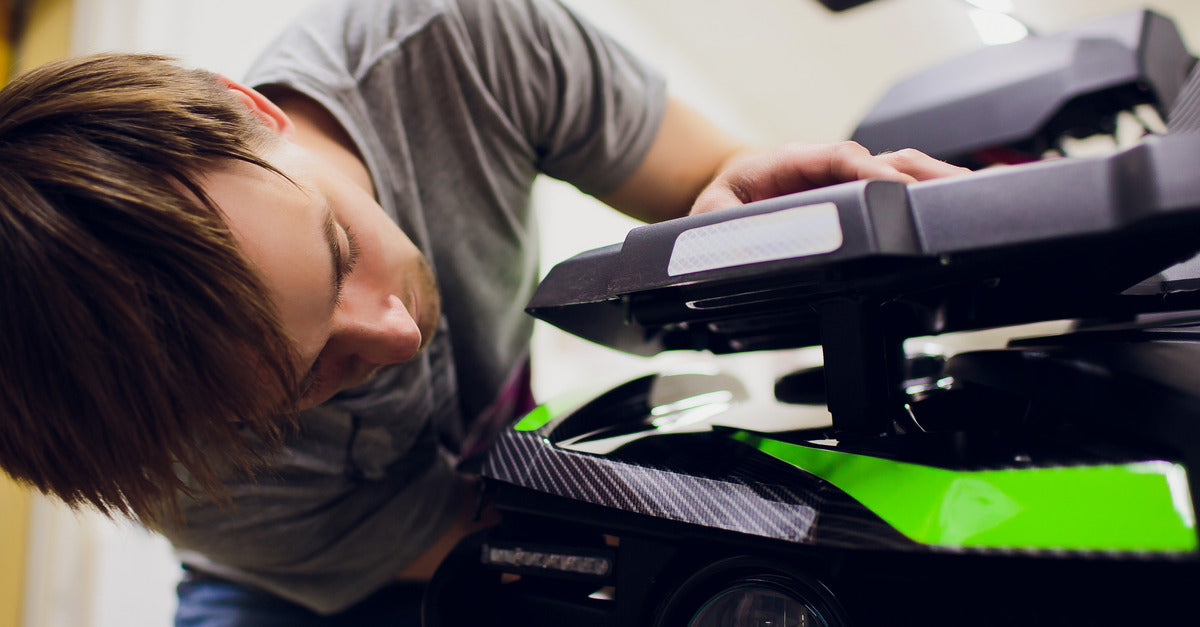 A young man inspects the internal components of an ATV between the crevice near the front of the vehicle.